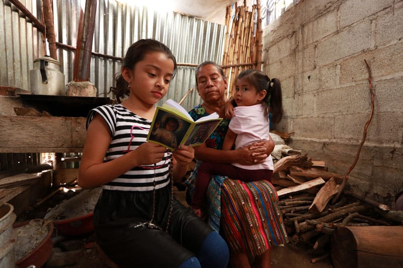 elderly lonely during pandemic: Cecilia Bixcul, 65, prays with her granddaughters in early July at her home in San Pedro, Guatemala. Bixcul attended Mass twice a week before COVID-19 put an end to that practice. (CNS photo/Oscar Tuc, Unbound.org)