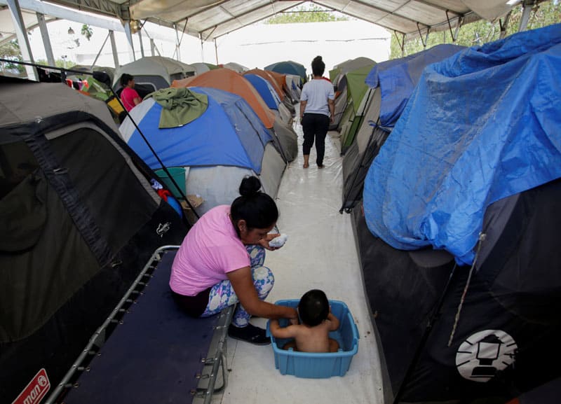 A migrant woman bathes her son outside their tent at a migrant encampment in Matamoros, Mexico, April 30, 2020, where more than 2,000 people live while seeking asylum in the U.S, as the spread of the coronavirus continues. (CNS photo/Daniel Becerril, Reuters)