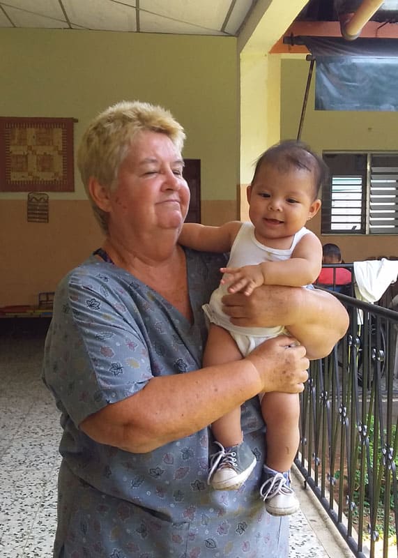 Dee-and-Sophie--in-text HIV COVID conference-Maryknoll Sister Delia Smith holds Sophie, the child of one of the hospice residents whom the Maryknoll sister is trying to keep free from COVID-19. (Courtesy of Delia Smith/Guatemala)