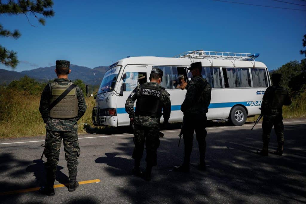 Members of Honduran security forces stand in front of a bus at a check point in Ocotepeque, Honduras, Dec. 10, 2020. The bus is carrying people taking part in a new caravan of migrants, set to head to the United States. (CNS/Jose Cabezas, Reuters)