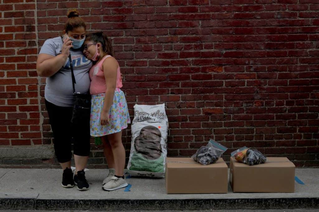 Sandra Cruz of Chelsea, Mass., waits for a ride with her daughter after picking up free groceries from a food pantry July 22, 2020. Cruz lost her job because of the coronavirus pandemic, fell four months behind on her rent and was fearing eviction. (CNS photo/Brian Snyder, Reuters)