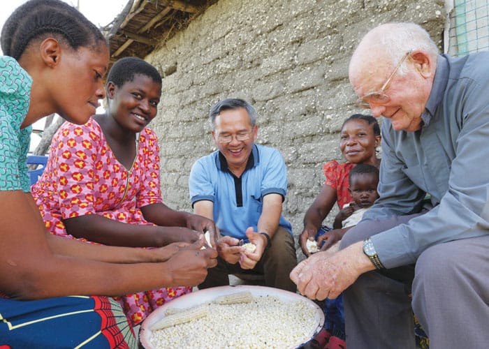 father-hung-1 Maryknoll Father Hung Dinh, center, and Father John Lange help a family in Ndoleleji parish remove dried corn kernels from their cobs in Shinyanga Diocese in Tanzania.