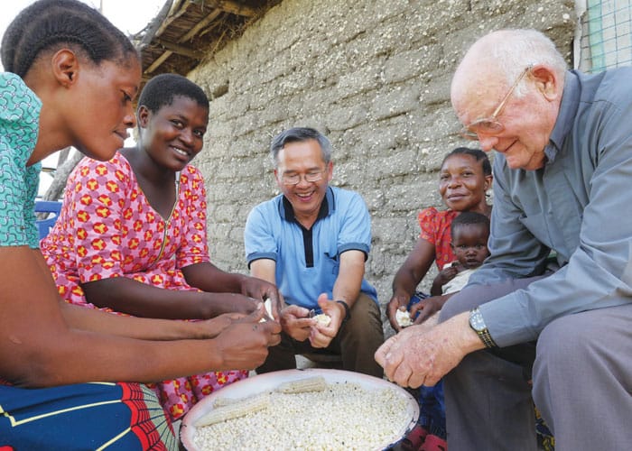 Maryknoll Father Hung Dinh, center, and Father John Lange help a family in Ndoleleji parish remove dried corn kernels from their cobs in Shinyanga Diocese in Tanzania.