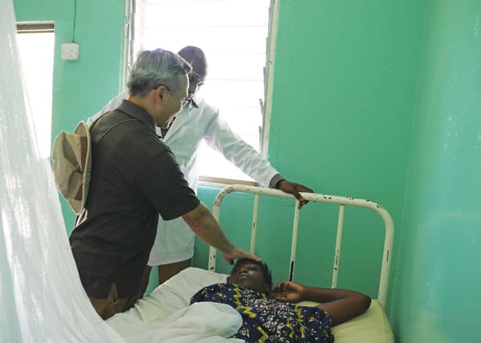 Father Dinh blesses an ailing woman while making rounds with a clinical officer at the Ndoleleji medical clinic and dispensary that treats about 40 patients a week.