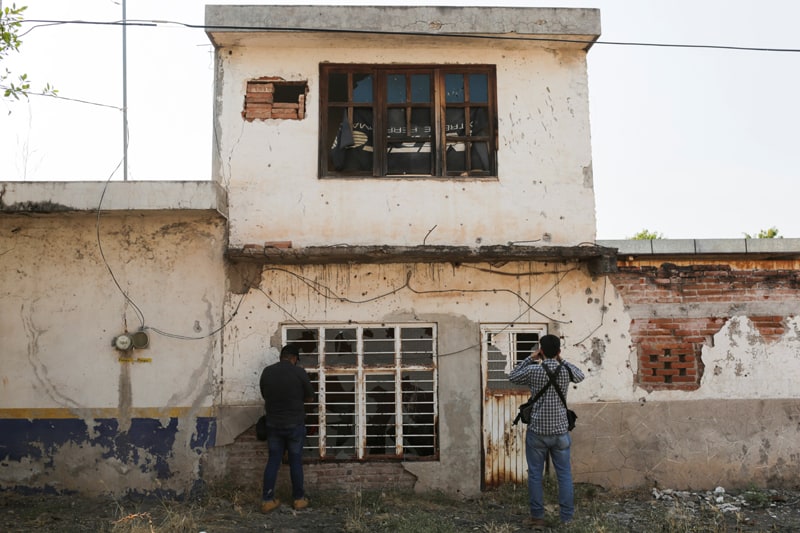 BESIEGED MEXICAN TOWN Photographers take pictures of the bullet-riddled front of an abandoned house near Aguililla, Mexico, April 23, 2021. Drug cartels have battled each other and blocked highways in the town, leaving residents unable to travel freely and causing shortages of everything from food to fuel. (CNS photo/Alan Ortega, Reuters)