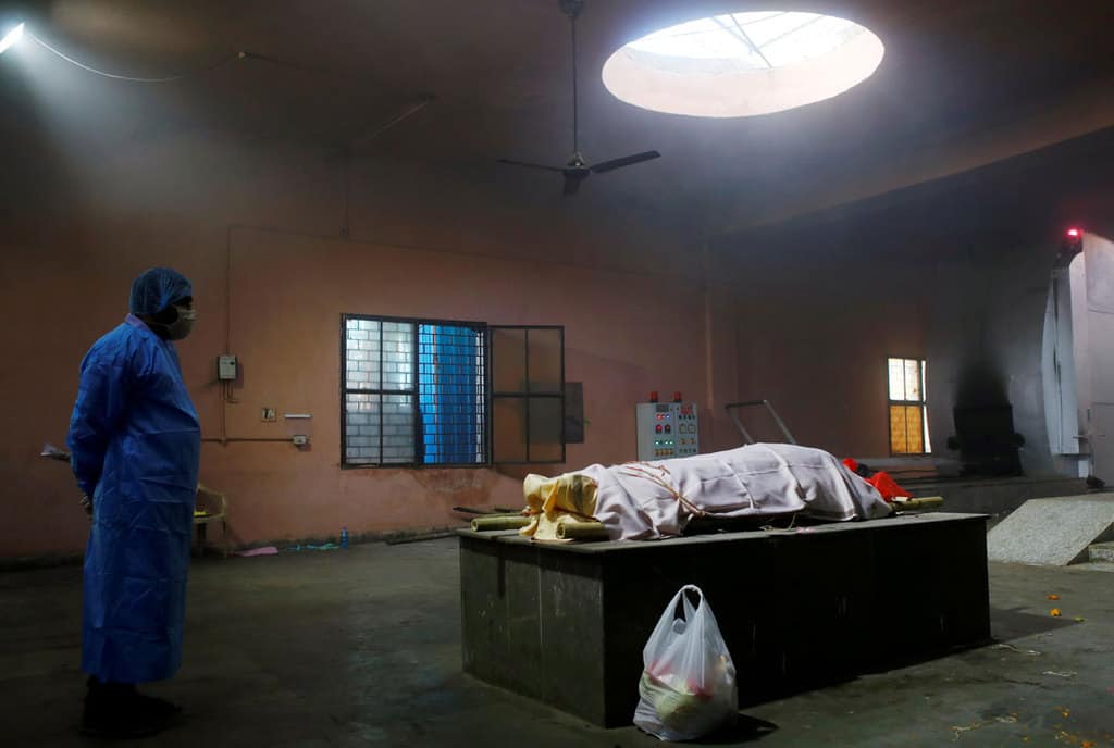 A family member wearing personal protective equipment stands next to the body of a woman before her cremation at a crematorium in New Delhi April 24, 2021. The woman died after contracting COVID-19. (CNS photo/Adnan Abidi, Reuters)