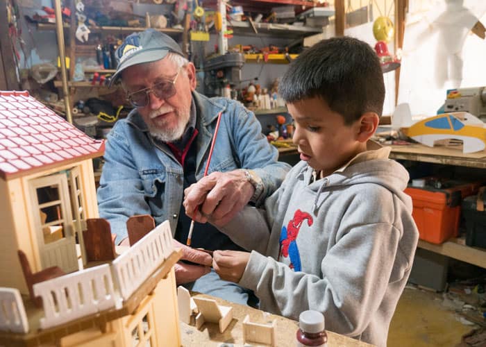 Web-Only-Sim-07 Father Paul Sykora, who runs the after-school tutoring program in Cochabamba, Bolivia, teaches a boy how to paint a toy house. (Nile Sprague/Bolivia)
