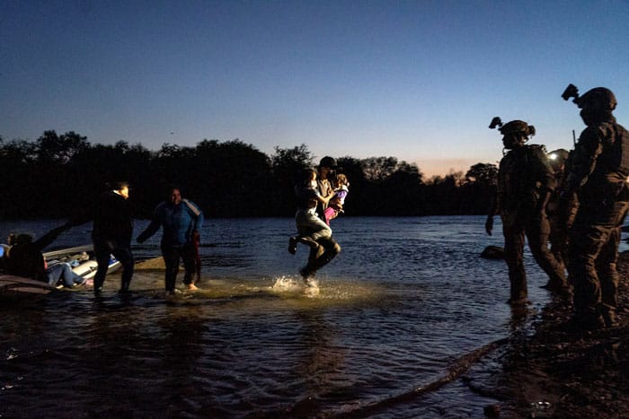 An asylum-seeking migrant carries two girls while walking in the Rio Grande as Texas Ranger officers await at the riverbank in Roma, Texas, April 5, 2021. (CNS photo/Go Nakamura, Reuters)