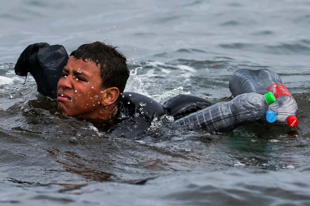 A Moroccan boy swims using bottles as a float, near the fence between the Spanish-Moroccan border, after thousands of migrants swam across the border, in Ceuta, Spain, May 19, 2021. In a statement released May 18, the Spanish bishops' conference expressed concern that migrants were being exploited after a sudden of influx of refugees into the Spanish territories of Ceuta and Melilla increased tensions between Spain and Morocco. (CNS photo/Jon Nazca, Reuters)