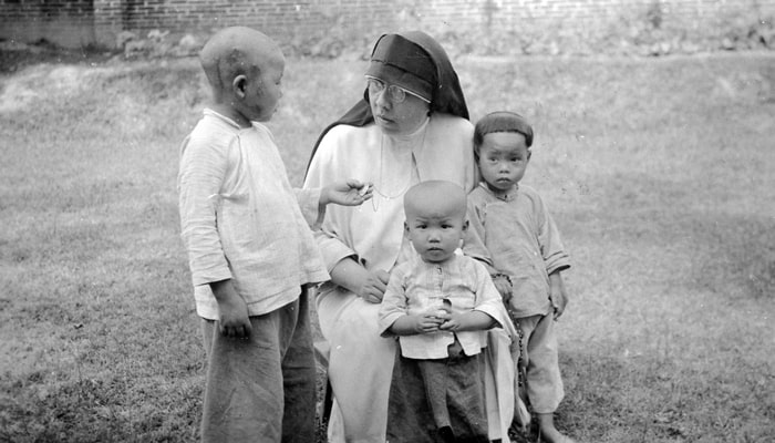 In Loting in 1938, Sister Francis Davis, a member of the second group of sisters sent to China, shares her faith with three girls, one of whom admires her medal. (Maryknoll Mission Archives)