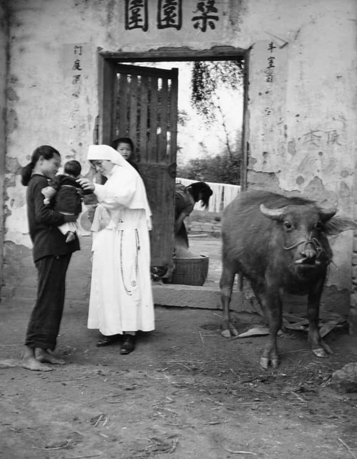 Sister Paulita Hoffmann, who died in 2019 after serving as a Maryknoll missioner for 85 years, greets a mother and childin Kaying, China, where she professed her final vows in 1939. (Maryknoll Mission Archives)