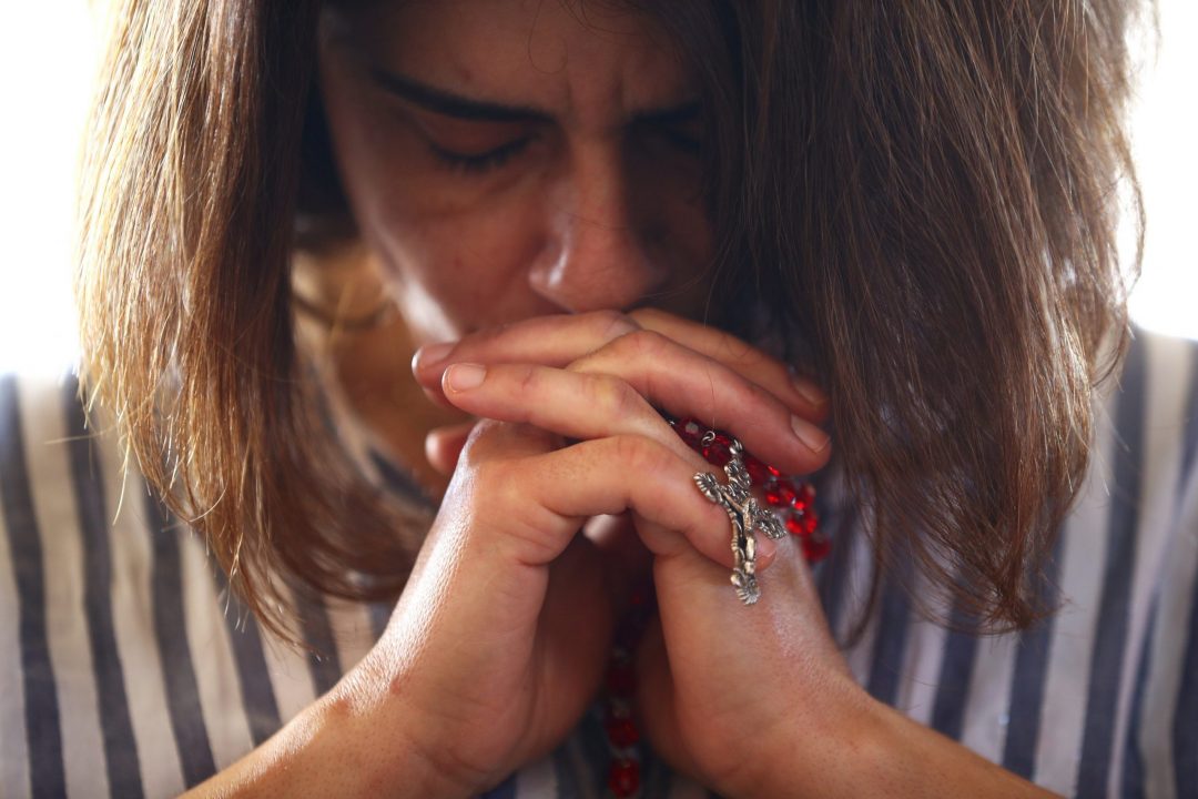 LEBANON PRAY EXPLOSION A woman holding a rosary prays during Mass at a church in Beirut Aug. 9, 2020. Lebanon's Christian advocates are urging that a special fund be established to address the continual flow of Christian emigration and to give them a solid reason to remain in their ancestral homeland. (CNS photo/Hannah McKay, Reuters)