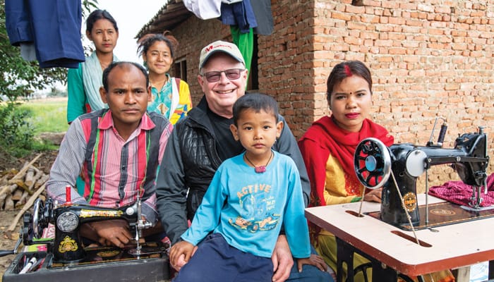 Father Thaler is flanked by Sitaram and Reena Tharu, graduates of the Sewing Cutting Training for Differently Abled Persons, as he visits their home. Trainees of the couple stand behind while a young neighbor sits with the Maryknoll priest. (Gregg Brekke/Nepal)