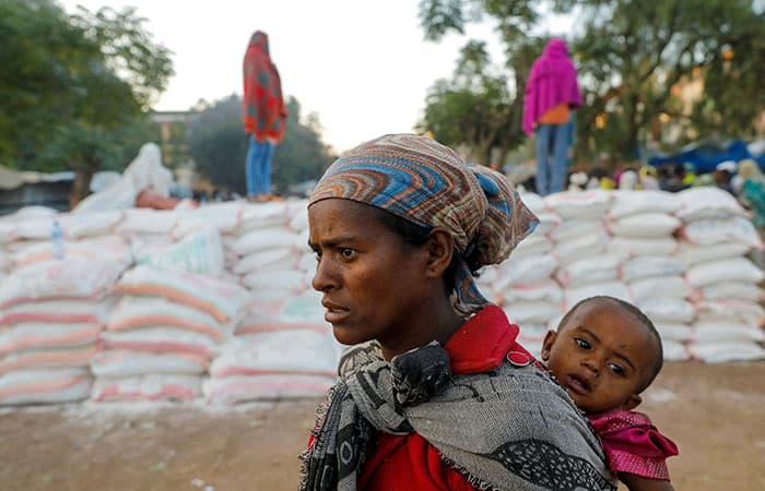 A woman carries an infant as she stands in line for food at the Tsehaye primary school, which was turned into a temporary shelter for people displaced by conflict, in the town of Shire, in Ethiopia's Tigray region, in this March 15, 2021, file photo. A new report from Refugees International echoes what Catholic leaders have been saying: The humanitarian situation in Tigray is abysmal. (CNS photo/Baz Ratner, Reuters)