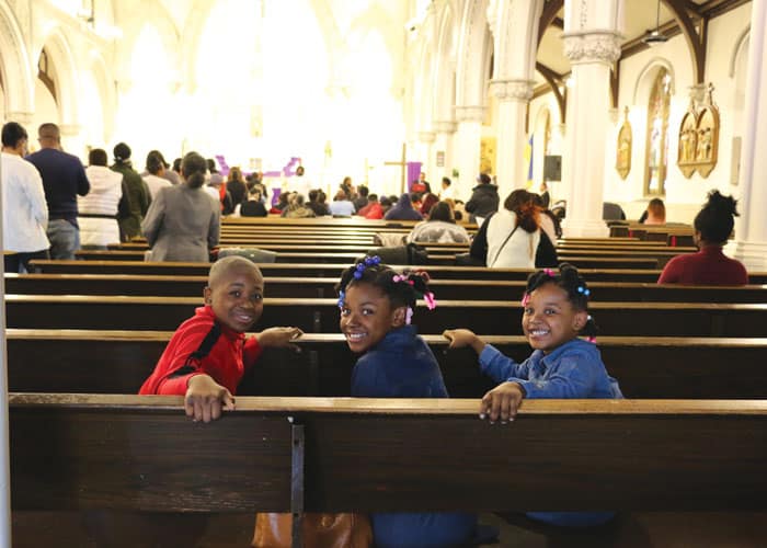 38-42-Fr-St-Vil-03 Anderson, Anchina and Briana Brice smile from the church pew as their parents, Andre and Ilna D. Brice, go up to receive Communion. (Diane Mastrogiulio/U.S.)