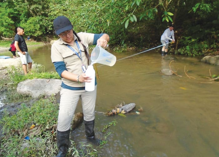 A technician from the national Ministry of the Environment and Natural Resources, Sol Muñoz, collects a river water sample while others take stream flow measurements. (Courtesy Margaret Vámosy)
