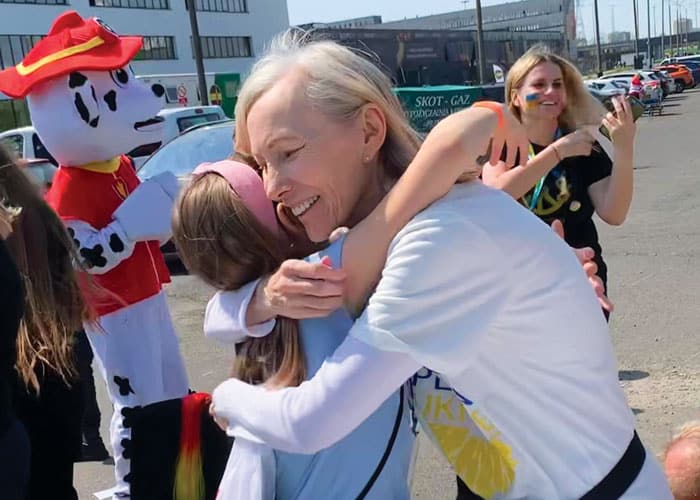 At a picnic, Maryknoll Affiliate Pam Cibik hugs a refugee child from Ukraine as volunteer coordinator Karolina Piskorz smiles in the background. (Courtesy Janet Alberti/Poland)