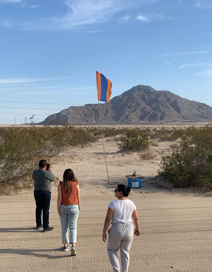 Young adults visiting migrant families see a water station for migrants crossing the border. The flag is located outside of Calexico just off of California State Route 98​, on the south side of the highway.