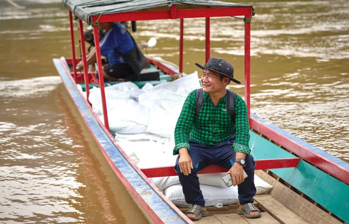 Pah Kler, a catechist who supervises shipping of food supplies to internally displaced people hiding in the forests of Myanmar, rides in a boat loaded with rice on the Salween River. (Paul Jeffrey/Thailand)