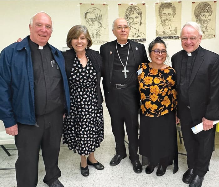 24-28-MKLM-Sending-Ceremony-03 Maryknoll Father Raymond Finch, Elvira Ramirez, Bishop Mark Seitz of El Paso, Sister Leonor Montiel and Father Lance Nadeau pose with portraits of the four churchwomen martyred in El Salvador at a reception held after the sending Mass and ceremony. (Courtesy of Maryknoll Lay Missioners/U.S.)